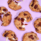 Salted Caramel Pecan New York Cookie with toasted pecans, caramelised white chocolate, and gooey salted caramel centre on pink background.
